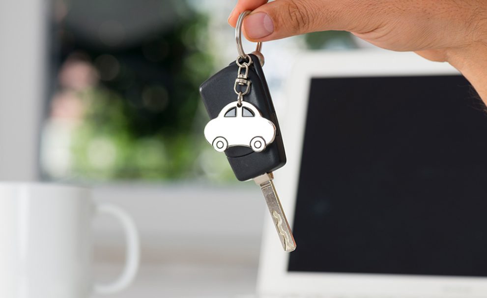 Hand holding a key with a car charm on it